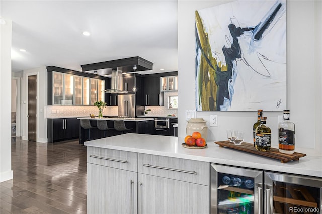 kitchen with decorative backsplash, dark cabinetry, wine cooler, and wall chimney exhaust hood