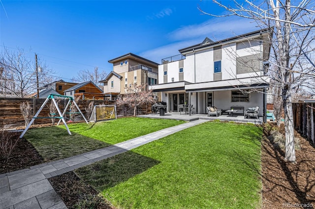 rear view of house with stucco siding, a fenced backyard, a playground, a yard, and a patio area