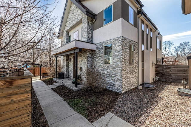 view of side of property with stone siding, stucco siding, a balcony, and fence