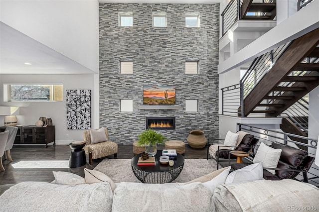 living room featuring baseboards, stairs, a fireplace, a towering ceiling, and wood finished floors