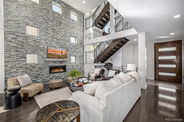 living area with dark wood finished floors, a stone fireplace, plenty of natural light, and stairs