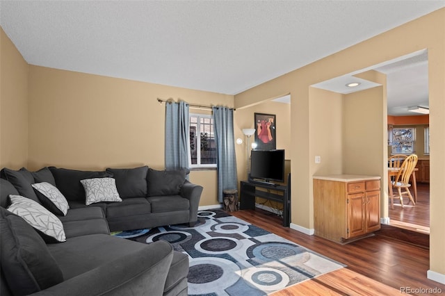 living area featuring a textured ceiling, dark wood finished floors, and baseboards