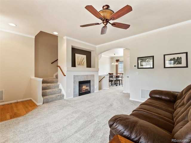 carpeted living area featuring crown molding, arched walkways, baseboards, and a ceiling fan