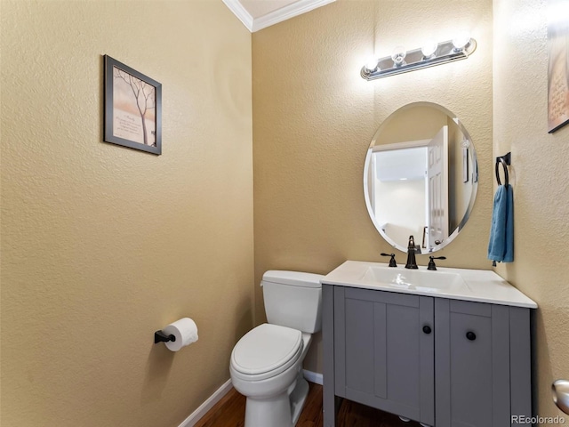half bathroom with crown molding, vanity, toilet, baseboards, and wood finished floors