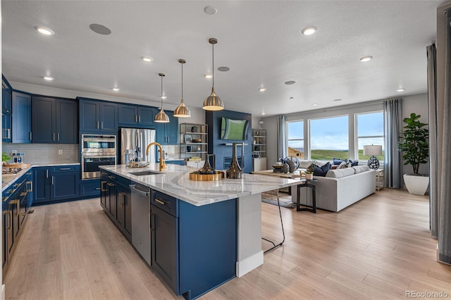 kitchen with stainless steel appliances, light hardwood / wood-style floors, decorative light fixtures, and a center island with sink