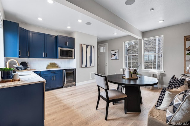 kitchen featuring blue cabinets, light wood-type flooring, beverage cooler, stainless steel microwave, and sink