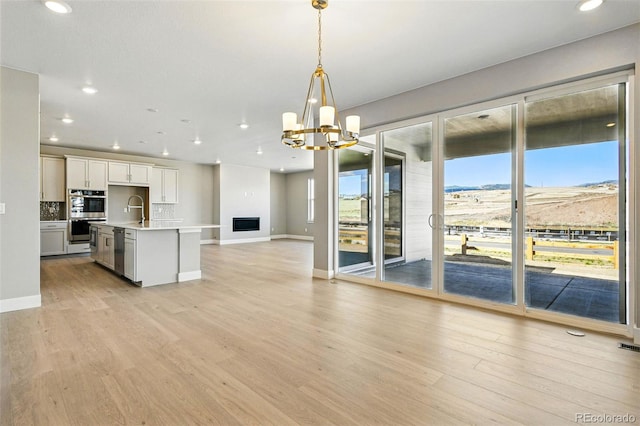 kitchen featuring open floor plan, an inviting chandelier, light wood-style floors, decorative backsplash, and appliances with stainless steel finishes