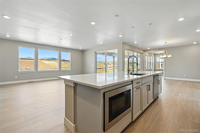 kitchen with a sink, stainless steel microwave, open floor plan, baseboards, and light wood-style floors