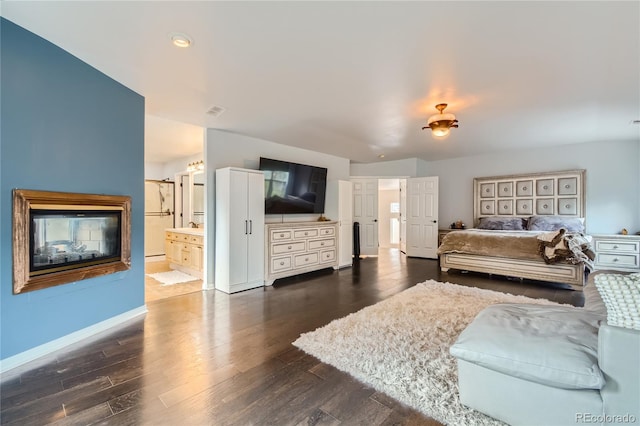 bedroom with baseboards, ensuite bathroom, freestanding refrigerator, and dark wood-type flooring