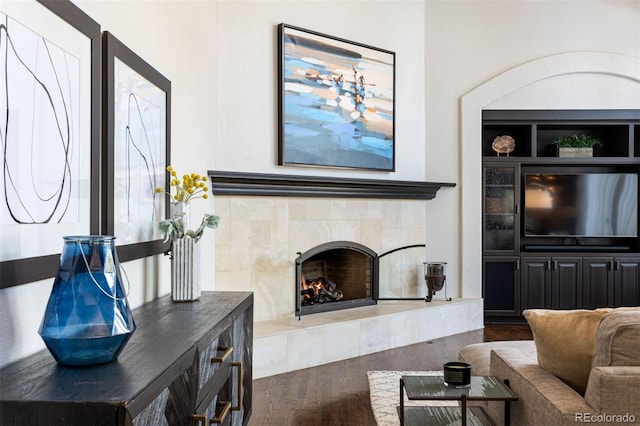 living room with a tile fireplace and dark wood-type flooring