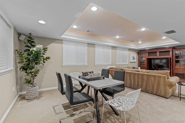 dining area with a tray ceiling and light colored carpet