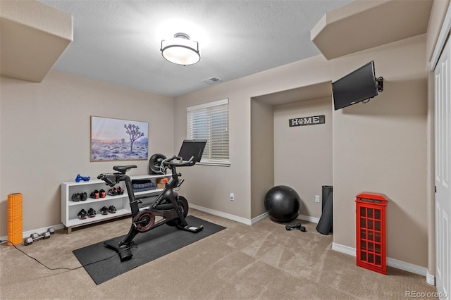 exercise area featuring light colored carpet and a textured ceiling