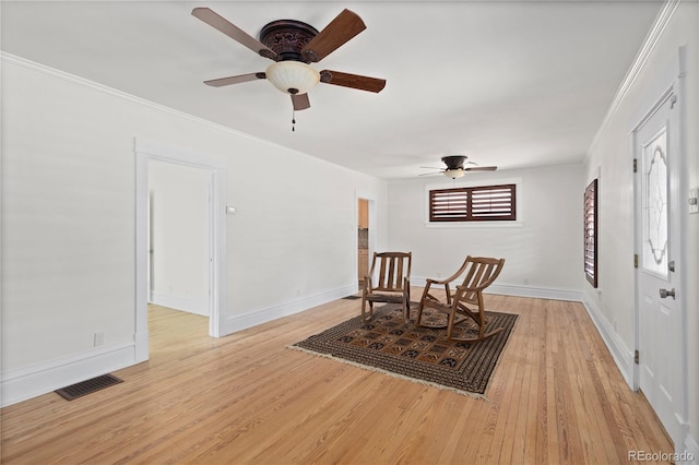 sitting room with light wood-type flooring, visible vents, and ornamental molding