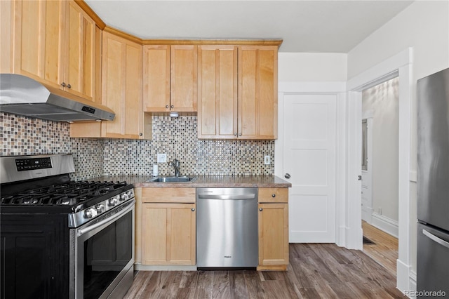 kitchen featuring under cabinet range hood, light brown cabinetry, wood finished floors, stainless steel appliances, and a sink