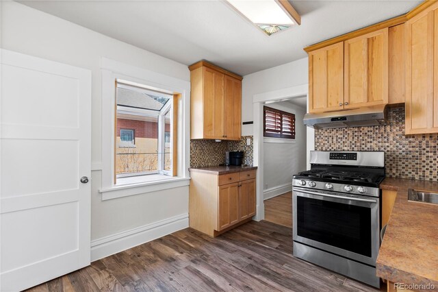 kitchen featuring baseboards, under cabinet range hood, stainless steel range with gas stovetop, dark wood finished floors, and decorative backsplash