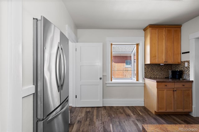 kitchen with tasteful backsplash, dark countertops, dark wood-type flooring, brown cabinets, and freestanding refrigerator