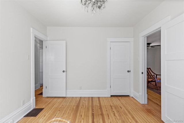 unfurnished bedroom with light wood-type flooring, visible vents, a closet, an inviting chandelier, and baseboards