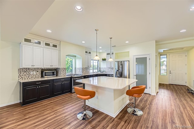 5495 Espana Ct, Denver, CO 80249 - kitchen with stainless steel appliances, white cabinetry, a kitchen bar, backsplash, and a kitchen island