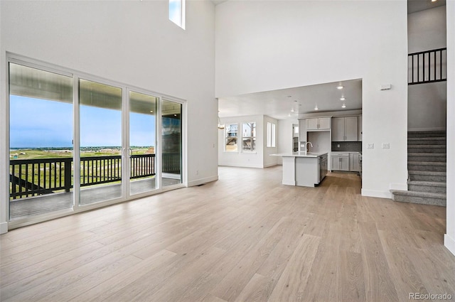 9382 Quaker St, Arvada, CO 80007 - unfurnished living room featuring a towering ceiling, light wood finished floors, stairway, baseboards, and a sink