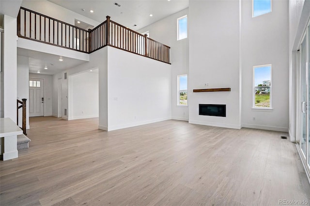 9382 Quaker St, Arvada, CO 80007 - unfurnished living room with a high ceiling, light wood finished floors, stairway, plenty of natural light, and a glass covered fireplace