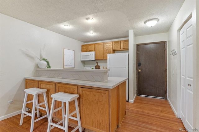 9650 Huron St Unit 12, Thornton, CO 80260 - kitchen with white appliances, a peninsula, light wood finished floors, a textured ceiling, and light countertops