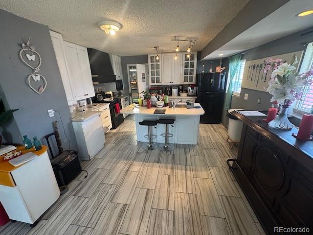 kitchen featuring black appliances, white cabinets, light countertops, and a kitchen island with sink