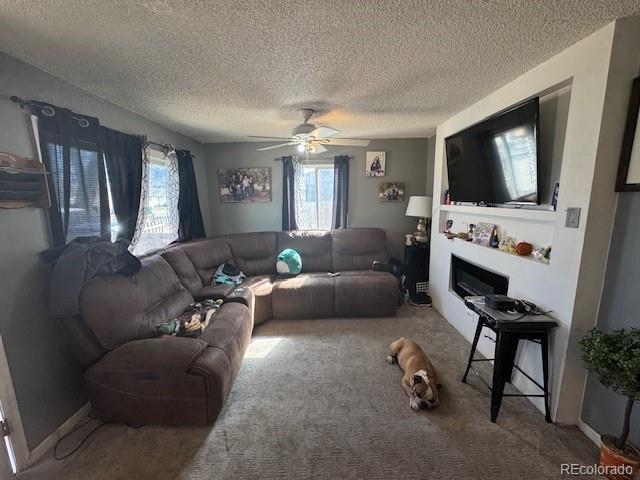 carpeted living room featuring a glass covered fireplace, a textured ceiling, and ceiling fan