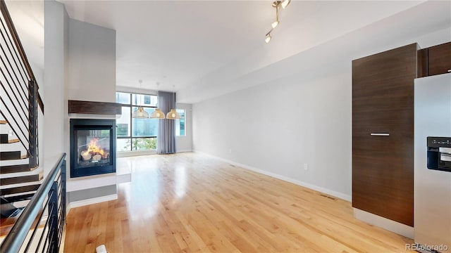 unfurnished living room featuring a multi sided fireplace, rail lighting, and light hardwood / wood-style floors