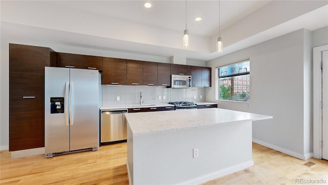 kitchen with a center island, hanging light fixtures, sink, appliances with stainless steel finishes, and dark brown cabinetry