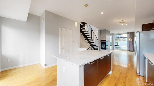 kitchen with pendant lighting, a multi sided fireplace, a center island, light hardwood / wood-style floors, and stainless steel refrigerator