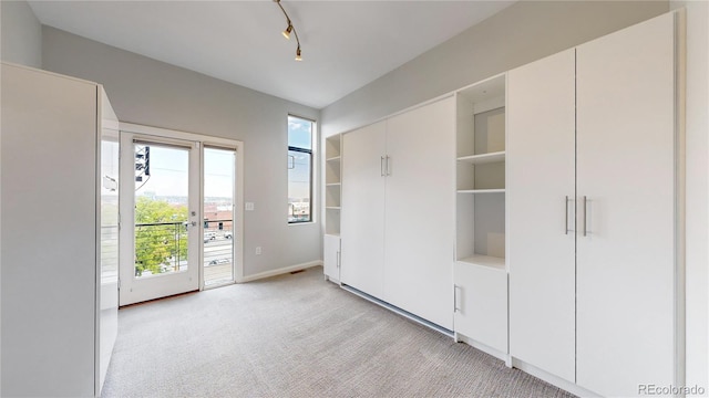 unfurnished bedroom with access to exterior, rail lighting, and light colored carpet