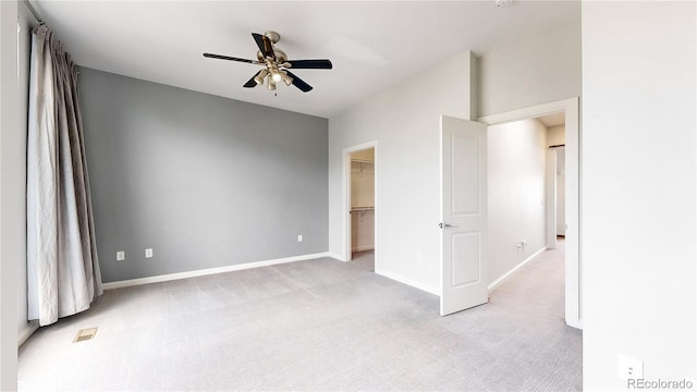 unfurnished bedroom with a spacious closet, a closet, ceiling fan, and light colored carpet