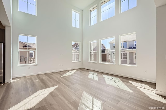 unfurnished living room with wood finished floors, visible vents, a towering ceiling, and baseboards