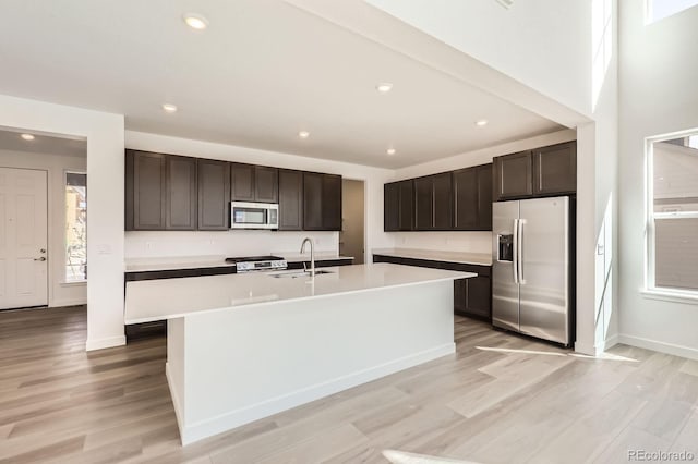 kitchen featuring stainless steel appliances, light countertops, dark brown cabinets, a sink, and light wood-style floors