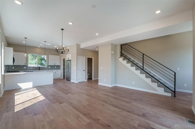 kitchen featuring pendant lighting, white cabinets, light hardwood / wood-style flooring, stainless steel refrigerator, and a chandelier