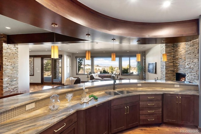 kitchen with a fireplace, decorative light fixtures, sink, light stone counters, and light hardwood / wood-style flooring