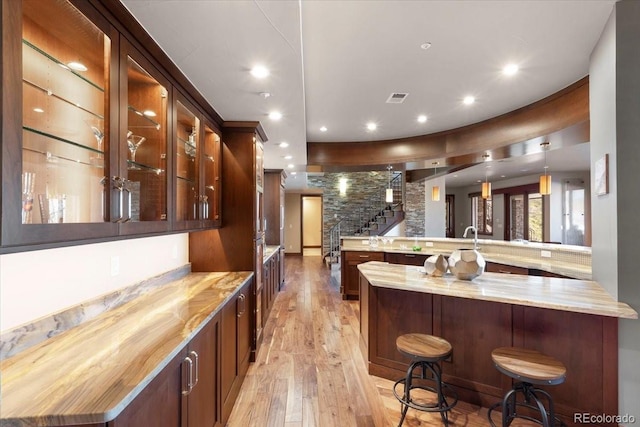 bar with decorative light fixtures, light stone countertops, and light hardwood / wood-style floors