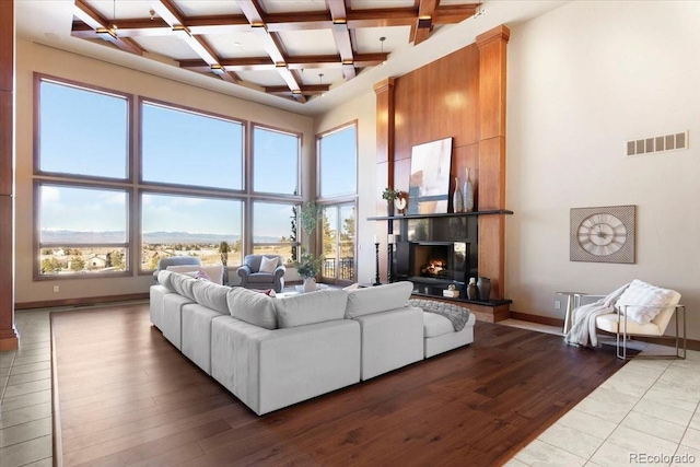 living room featuring a towering ceiling, wood-type flooring, coffered ceiling, and beam ceiling