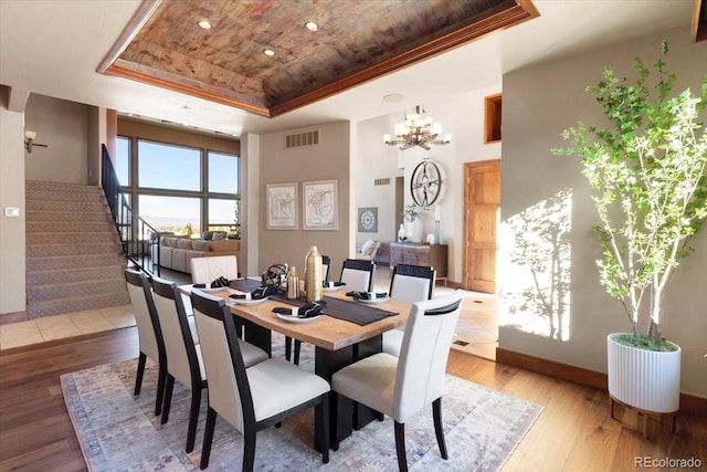 dining room featuring a raised ceiling, wood ceiling, an inviting chandelier, and light hardwood / wood-style flooring