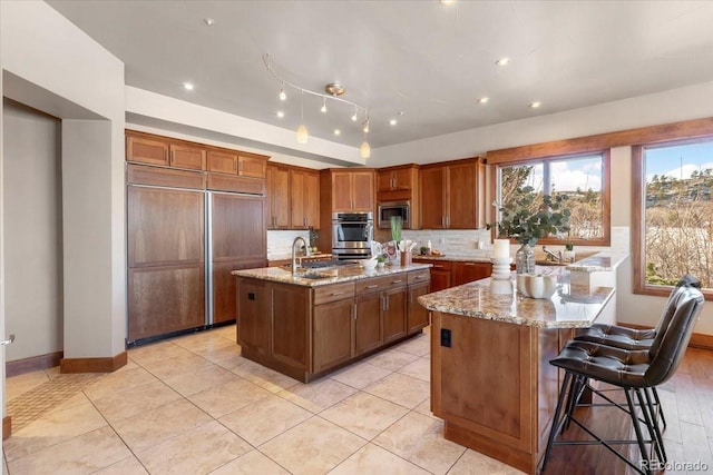 kitchen featuring an island with sink, sink, built in appliances, and light stone counters