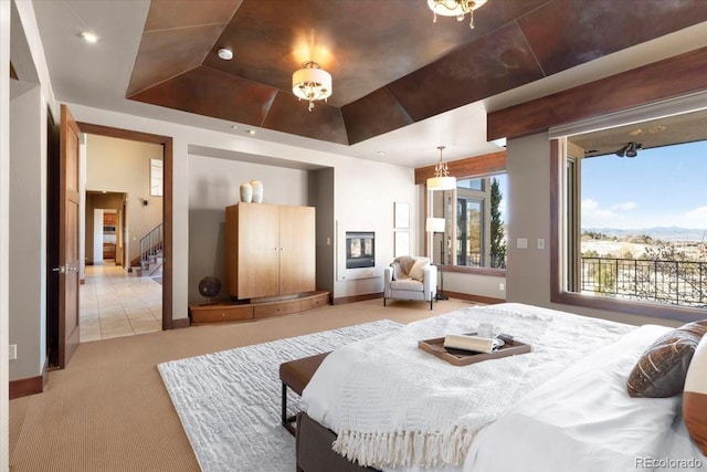 bedroom featuring light carpet, baseboards, access to exterior, a raised ceiling, and a glass covered fireplace