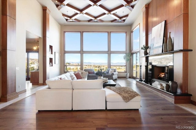 living room featuring baseboards, coffered ceiling, a towering ceiling, wood finished floors, and a fireplace