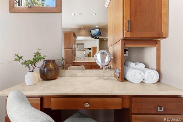 kitchen with light stone counters, built in desk, and brown cabinets