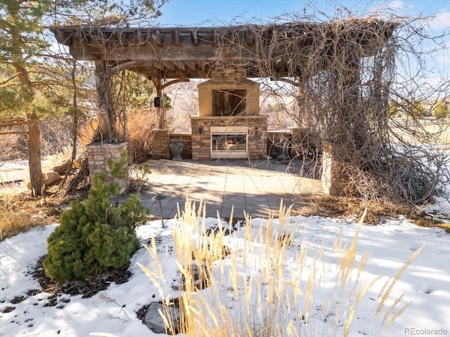 snow covered patio featuring an outdoor stone fireplace