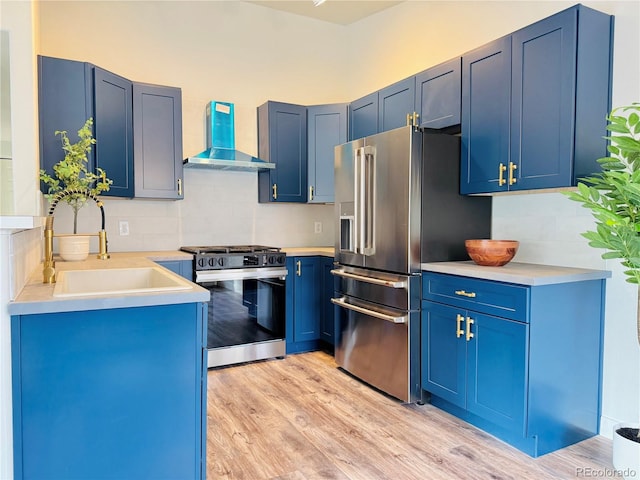 kitchen featuring blue cabinets, wall chimney exhaust hood, light wood-type flooring, and appliances with stainless steel finishes