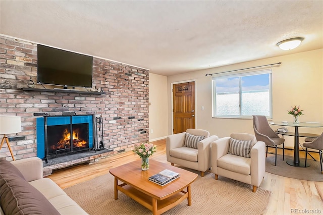 living area featuring a textured ceiling, a fireplace, baseboards, and wood finished floors