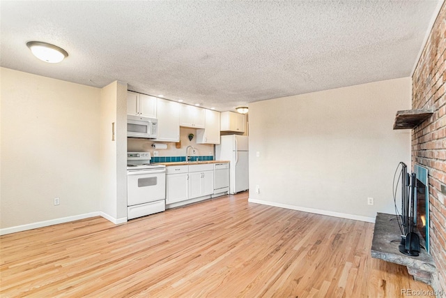 kitchen with white appliances, a sink, white cabinets, light wood-style floors, and a brick fireplace