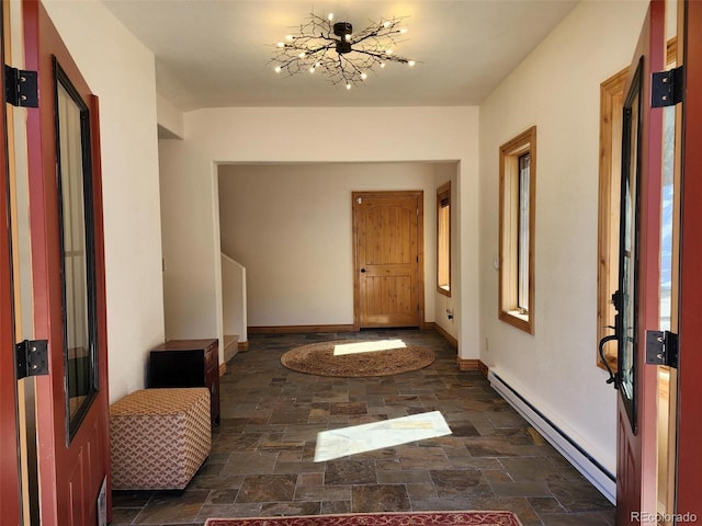 entryway featuring a notable chandelier, stone finish floor, a baseboard heating unit, and baseboards