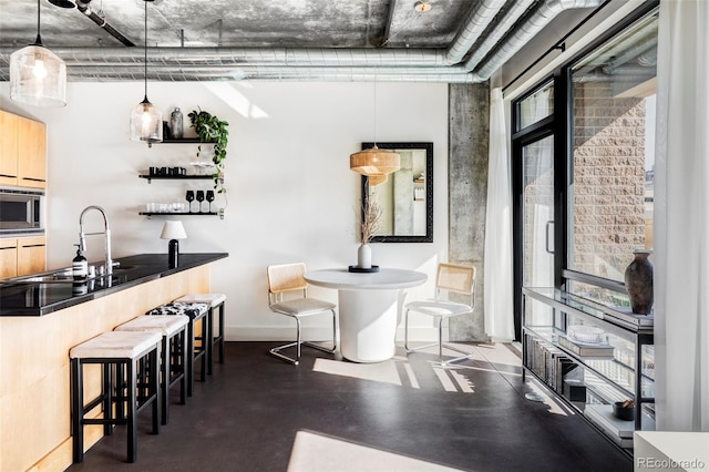 bar featuring a sink, concrete floors, baseboards, stainless steel microwave, and pendant lighting