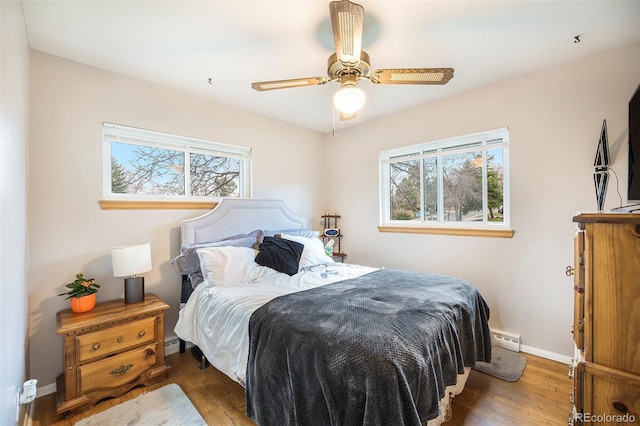 bedroom with baseboards, wood finished floors, baseboard heating, and multiple windows